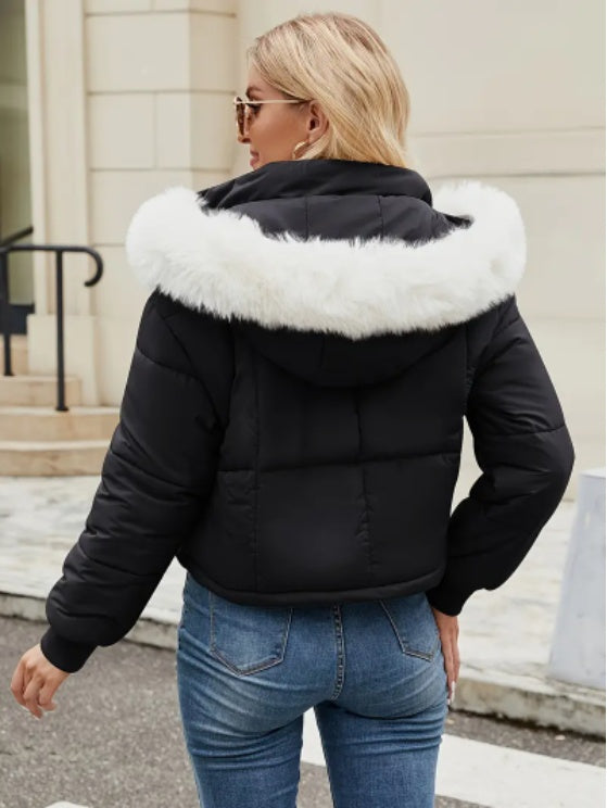 Woman wearing a black puffer jacket with white faux-fur hood trim outside.