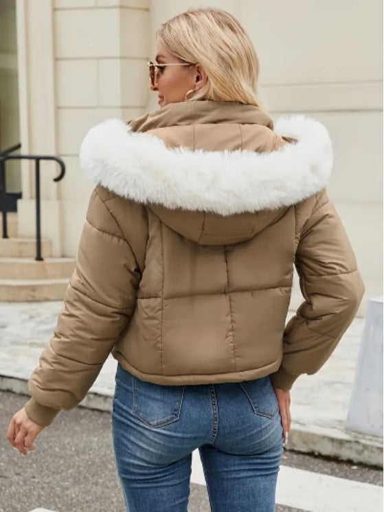 Woman wearing a beige puffer jacket with white fur trim outdoors.